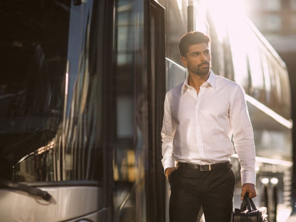 A professional male hospitality worker in a white formal shirt and black trousers holding a bag next to a staff transport bus, deployed by MSQ, a trusted hotel pre-opening manpower supplier in Qatar.