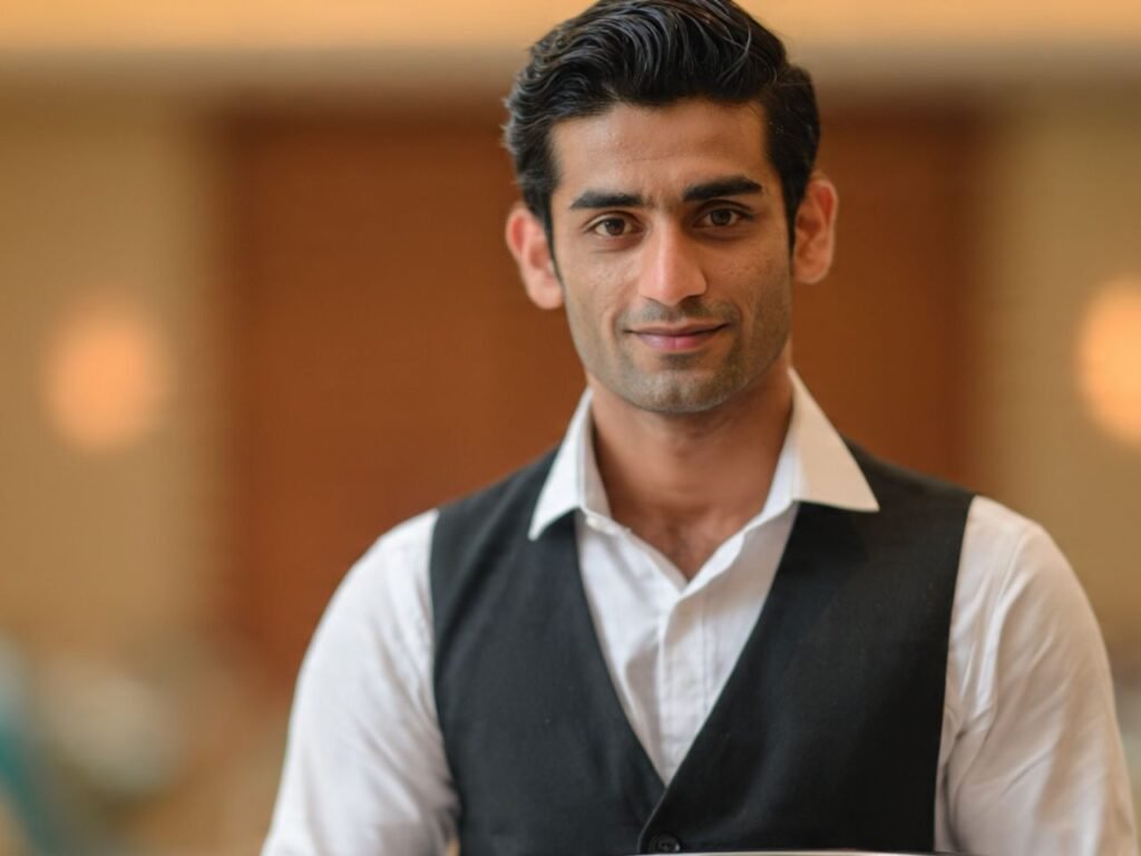 A professional male banquet waiter in a formal black vest and white shirt inside a luxury event venue, supplied by MSQ, a reliable event hospitality staff supplier in Qatar.