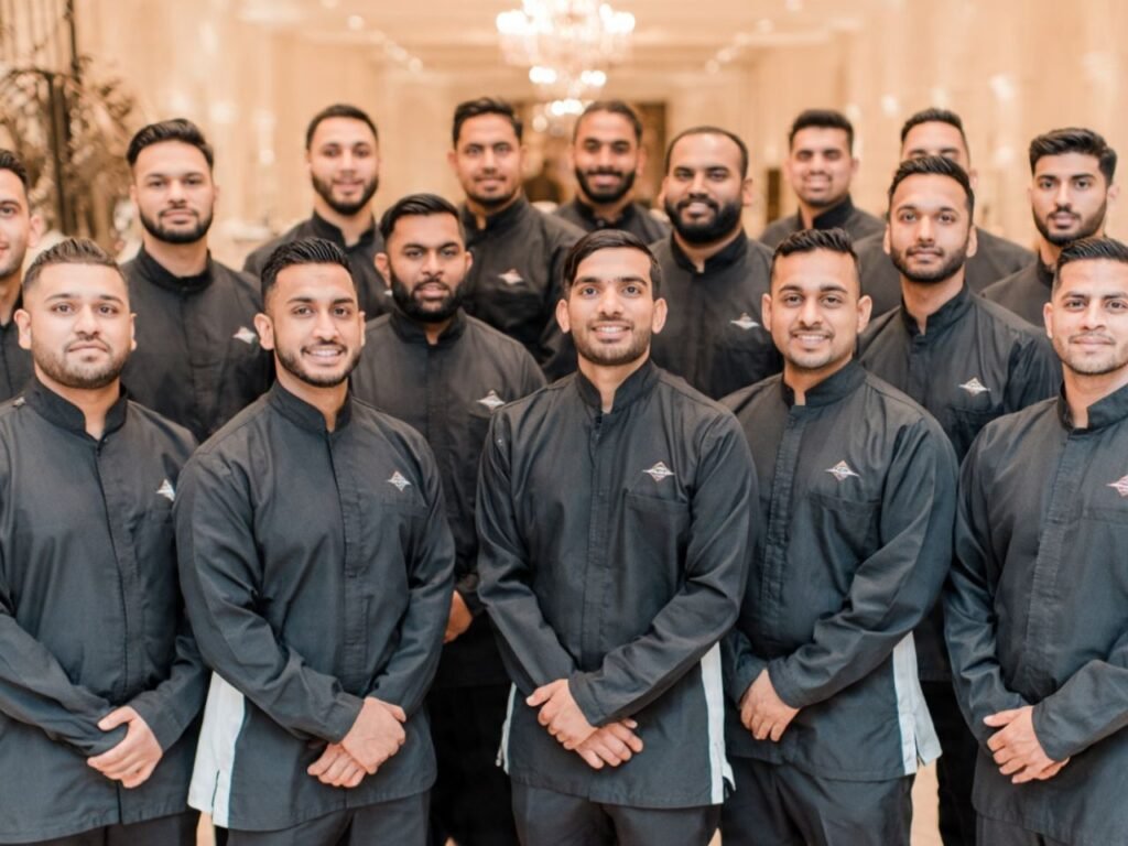 A large group of professional male hospitality staff standing in matching black uniforms inside a luxury event hall, deployed by MSQ, a leading event hospitality staff supplier in Qatar.